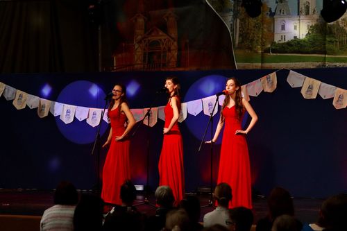 három piros ruhába öltözött lány énekel